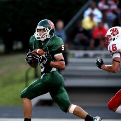 Football player running with ball in front of second player running behind with hands outstretched