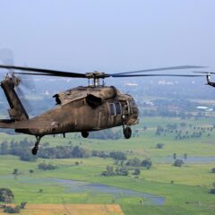 Two military helicopters in flight over landmass with one helicopter closeup shot